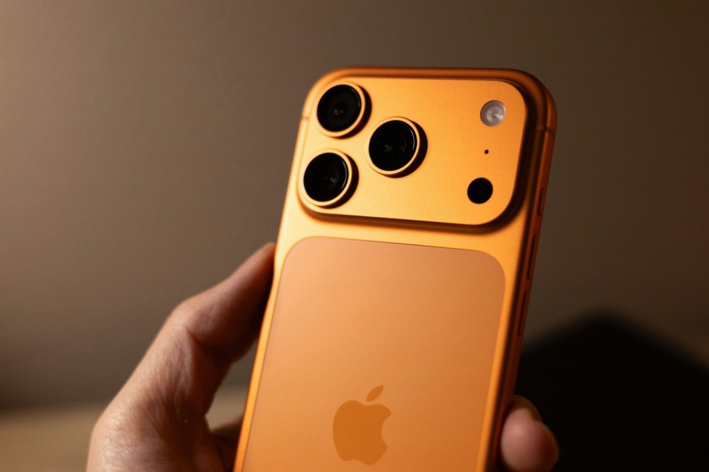 Back of an orange iPhone with a three-lens camera, held in one hand